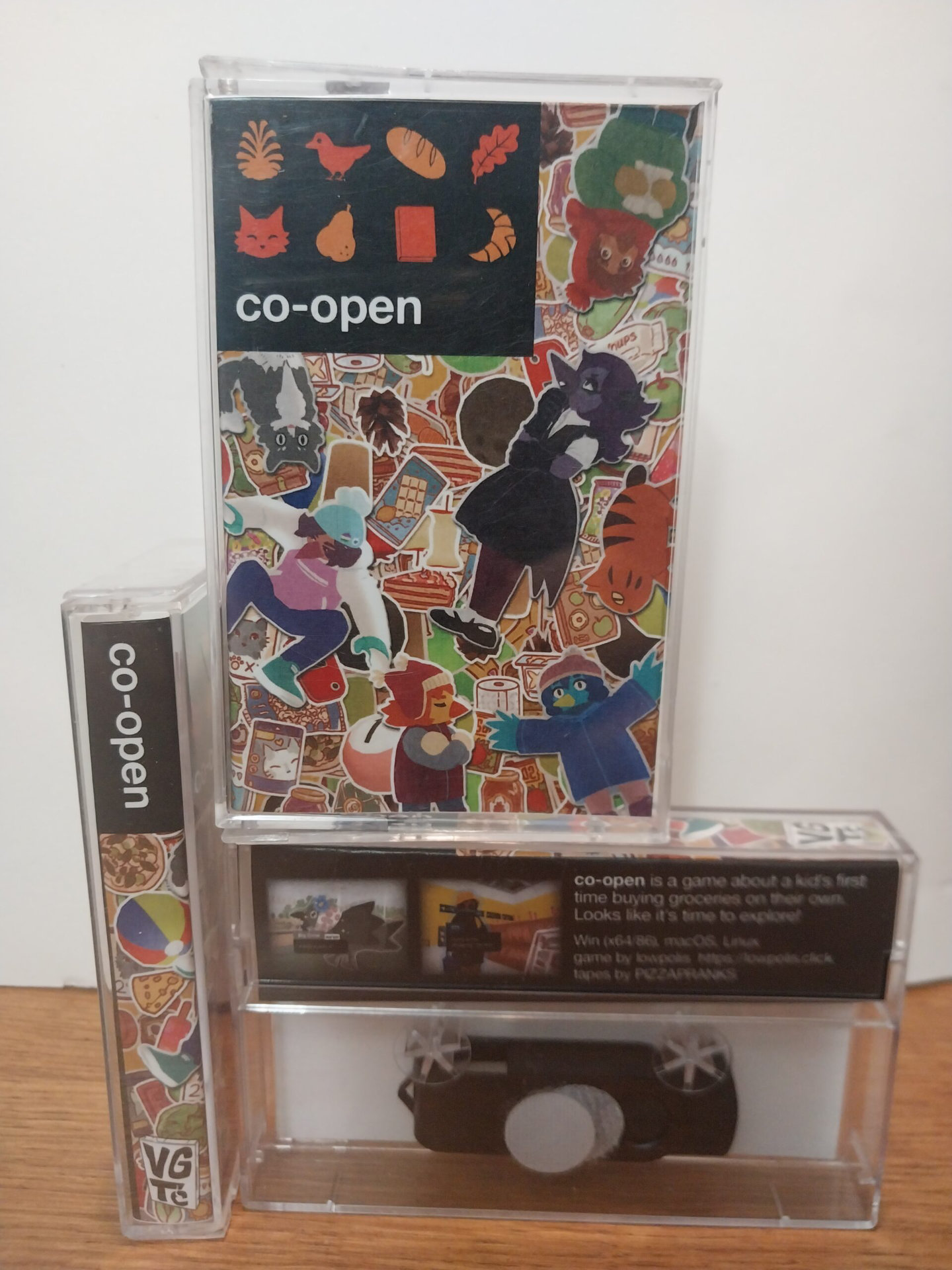 A photo of cassette tape cases on a table with various characters and items from the video game "co-open" featured on their covers as stickers applied on top of each other.
